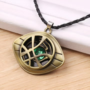 Gold pendant with green gemstone on a black cord, placed on a wooden surface.